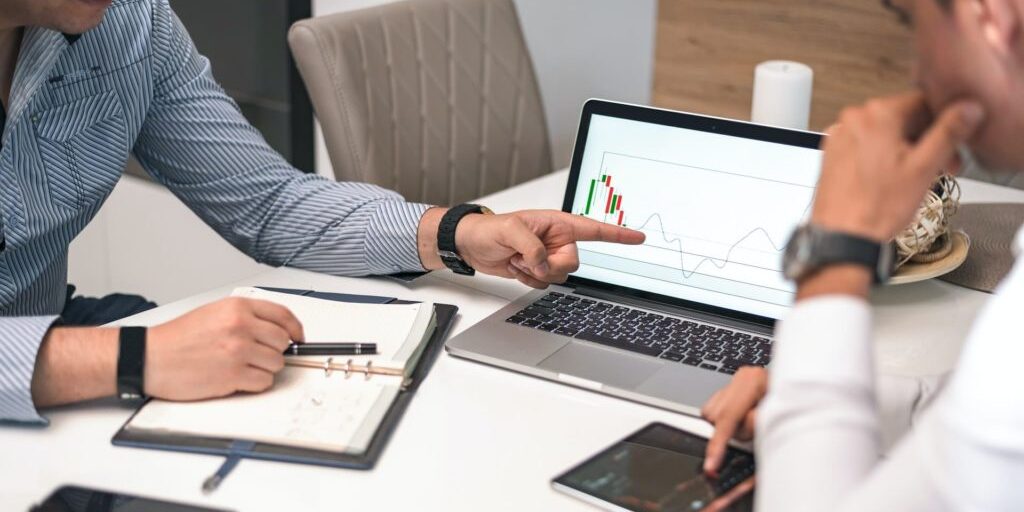 banner_mercado Duas pessoas analisando gráficos de mercado